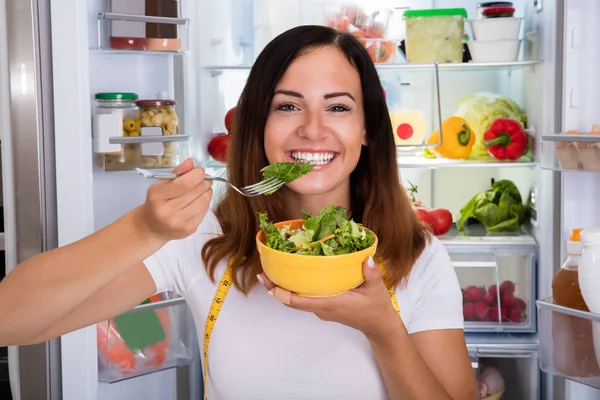 Woman eats in front of refrigerator — Stock Photo, Image