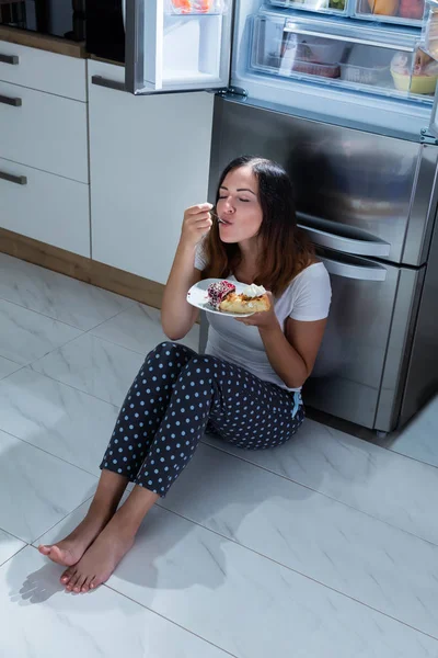 Woman eats in front of refrigerator — Stock Photo, Image