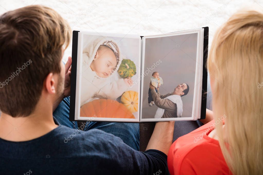 High Angle View Of Young Couple Looking At Photo Album