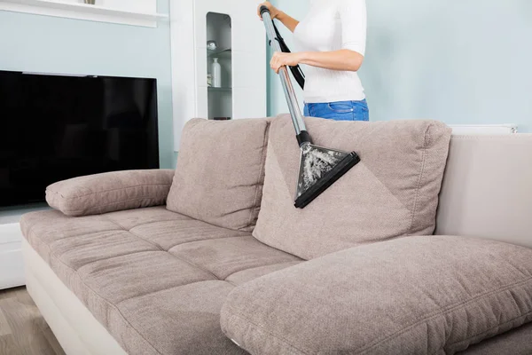 Женщина чистит диван с пылесосом — стоковое фото