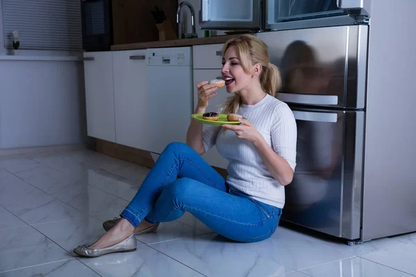 Frau isst süßes Essen in der Nähe des Kühlschranks — Stockfoto