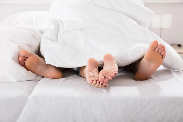 Male and female legs under bed sheet — Stock Photo, Image