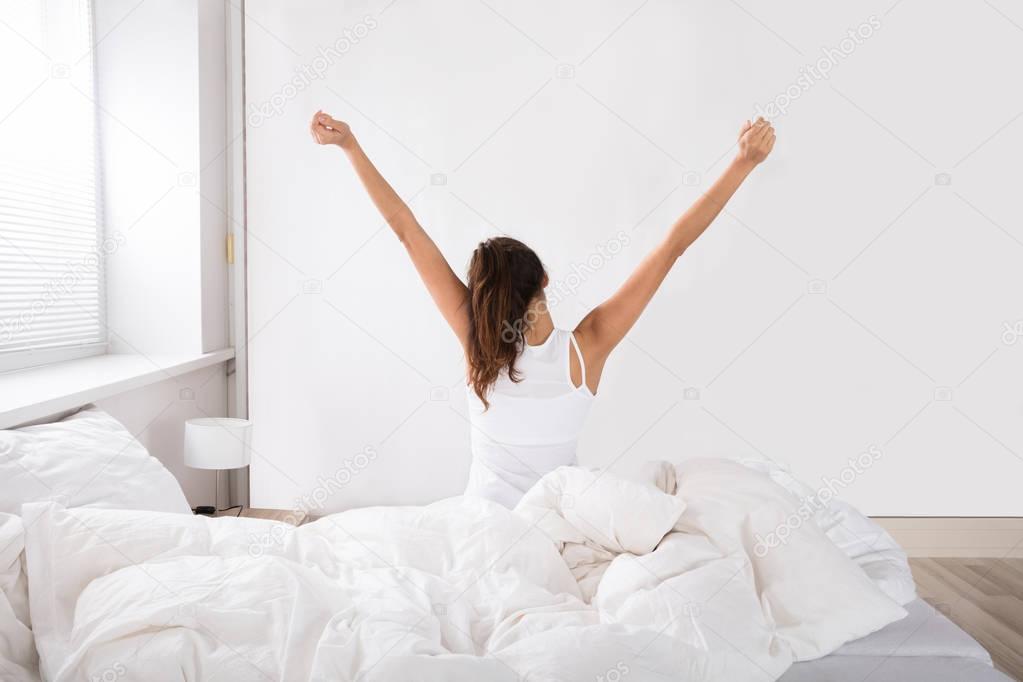 woman stretching arms in bed
