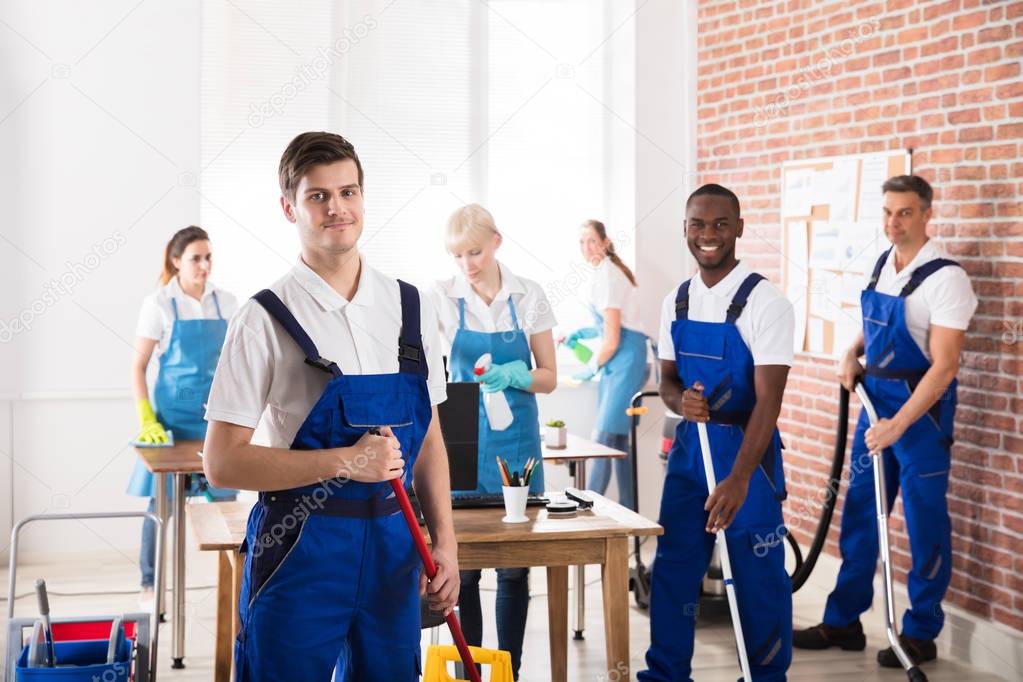 Group Of Diverse Janitors In Uniform Cleaning The Office With Cleaning Equipments