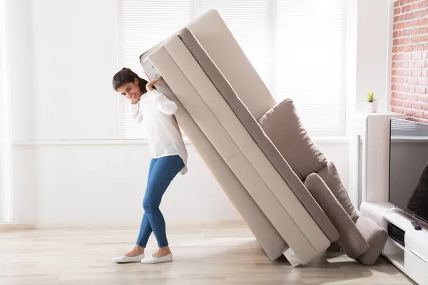 Woman trying to move sofa at home — Stock Photo, Image