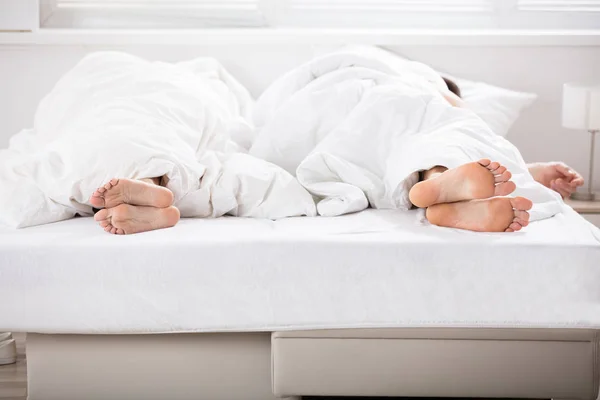 Mannelijke en vrouwelijke benen onder bed vel — Stockfoto