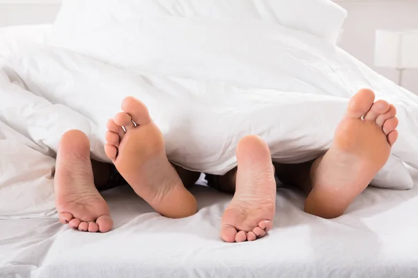 Mannelijke en vrouwelijke benen onder bed vel — Stockfoto