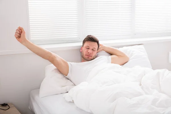 Homem esticando as mãos na cama — Fotografia de Stock