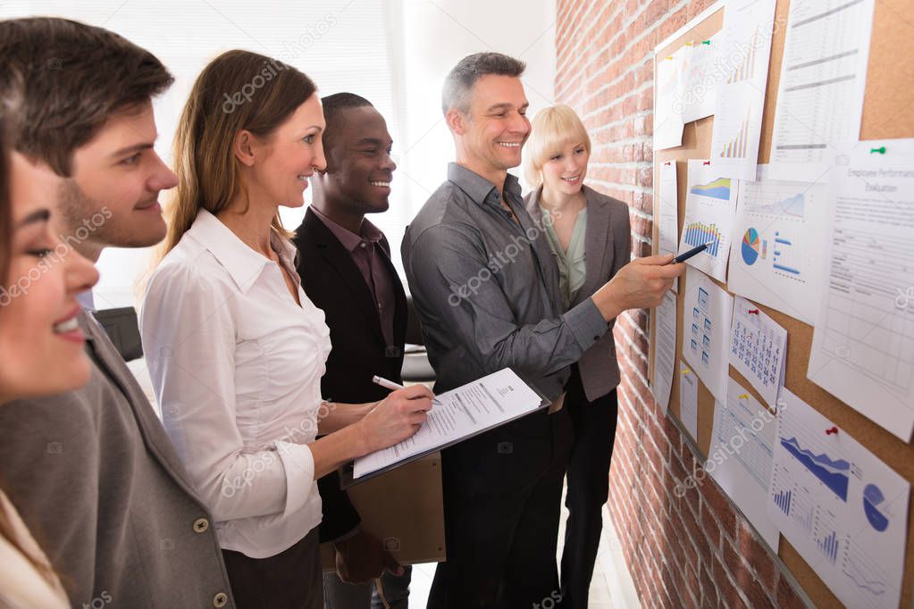 Mature Manager Analyzing The Graph With His Colleague Attached On Bulletin Board