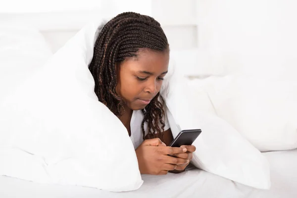 Dziewczyna w łóżku przy użyciu telefonu komórkowego — Zdjęcie stockowe