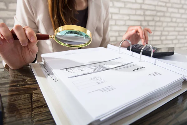 Businesswoman examining invoices with magnifying glass — Stock Photo, Image