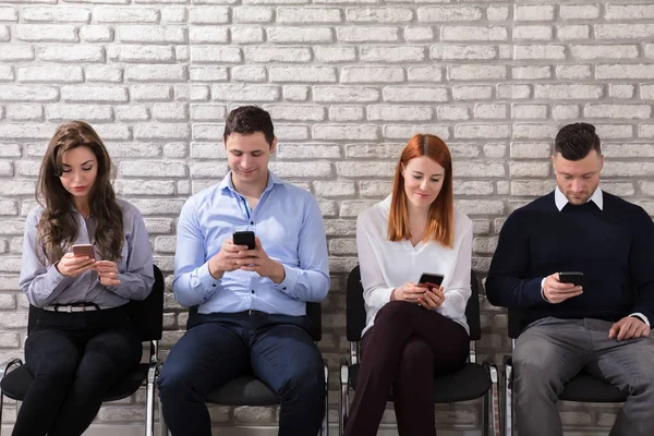 Giovani Uomini Affari Seduti Sulla Sedia Utilizzando Telefono Cellulare Contro — Foto Stock