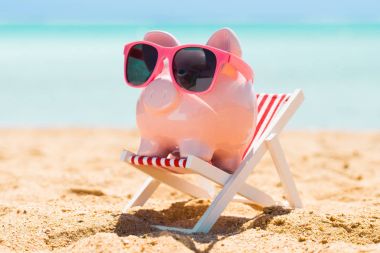 Plajda küçük şezlong üzerinde güneş gözlüğü ile pembe Piggy banka