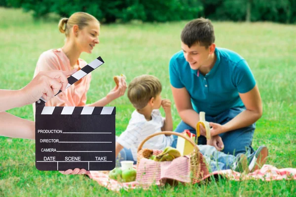 Hands Holding Clapperboard While Young Family Enjoying Picnic Grassy Field — Stock Photo, Image