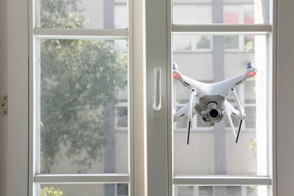 Fliegender weißer Quadrocopter spioniert durch Fenster eines Hauses — Stockbild Fliegender weißer Quadrocopter — Stockfoto