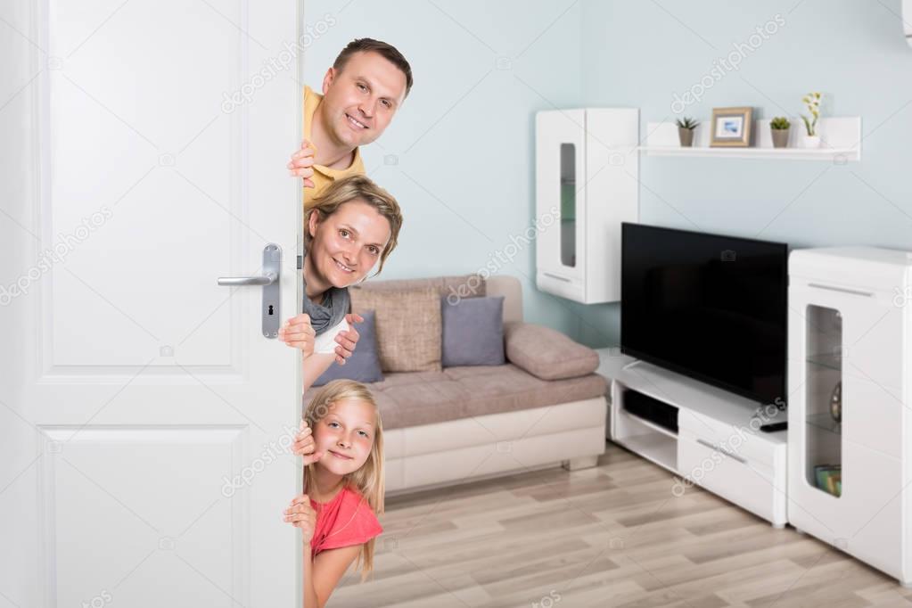 Portrait Of Happy Family Peeking From Door In Living Room
