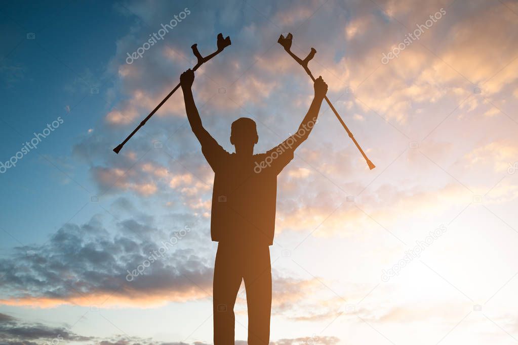 Silhouette Of Disabled Man Holding Crutches Against Dramatic Sky