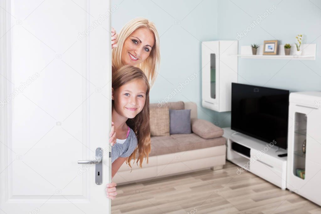 Portrait Of Happy Mother And Daughter Peeking From Door