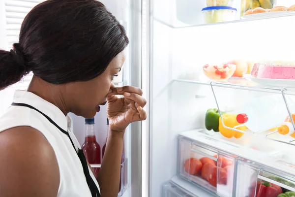 Frau hält Nase in der Nähe von verschmutztem Essen im Kühlschrank — Stockfoto