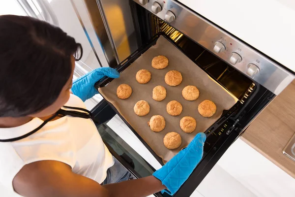 Женщина вытаскивает поднос с печеньем из духовки — стоковое фото