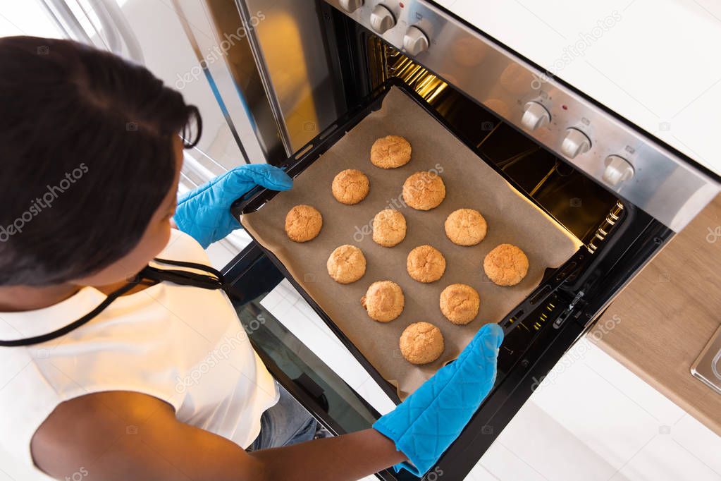 Woman Taking Out Tray Of Baked Cookies From Oven