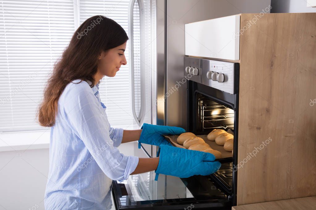 Woman Taking Out Tray Of Baked Bread From Oven 