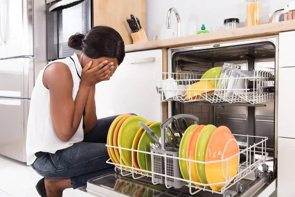 Mulher agachado perto de máquina de lavar louça — Fotografia de Stock