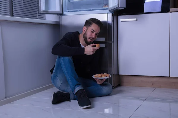 Homem sentado no chão comer biscoito — Fotografia de Stock