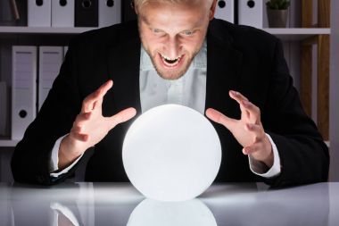 Young Businessman Looking Into The Future In A Crystal Ball In Office clipart