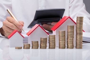 İş adamının farklı boyutlarda evleri ve para yığınlarıyla faturaları hesaplarken yakın plan fotoğrafı.