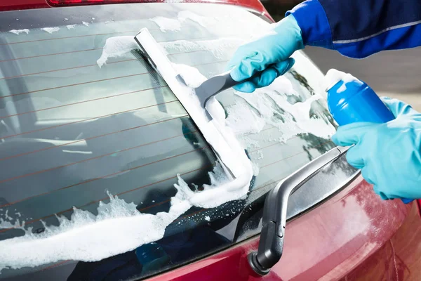 Close-up Of Person\'s Hand Washing Rear Windshield Of A Car Using Squeegee