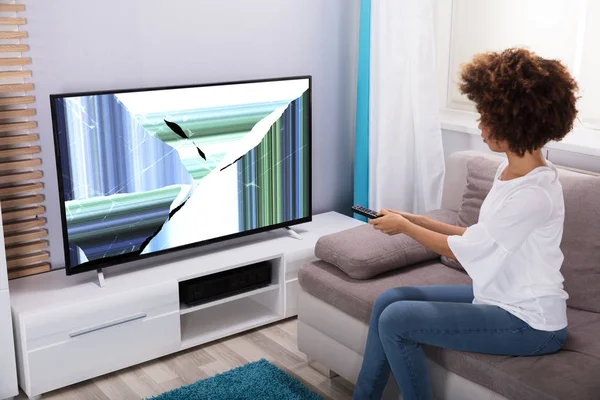 Young Woman Sitting On Sofa Near Television Showing Distorted Screen