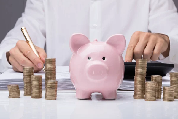 Крупный План Бизнесмена Рассчитывающего Законопроект Помощью Piggybank Укладываемых Монет Столе — стоковое фото