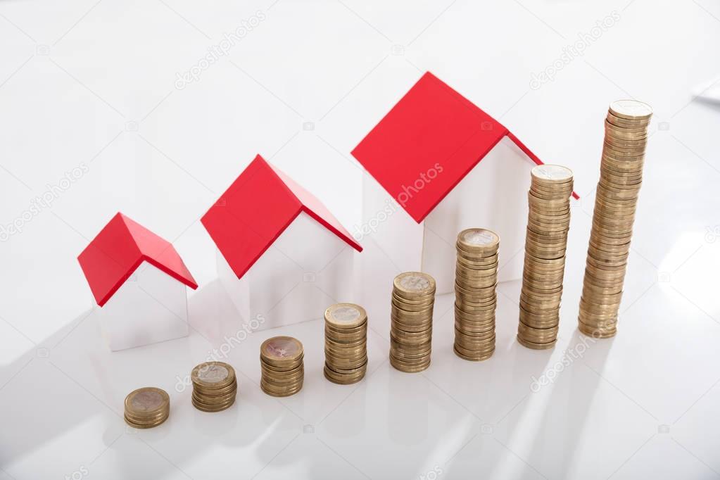 Elevated View Of House Models And Stack Of Coins On White Desk