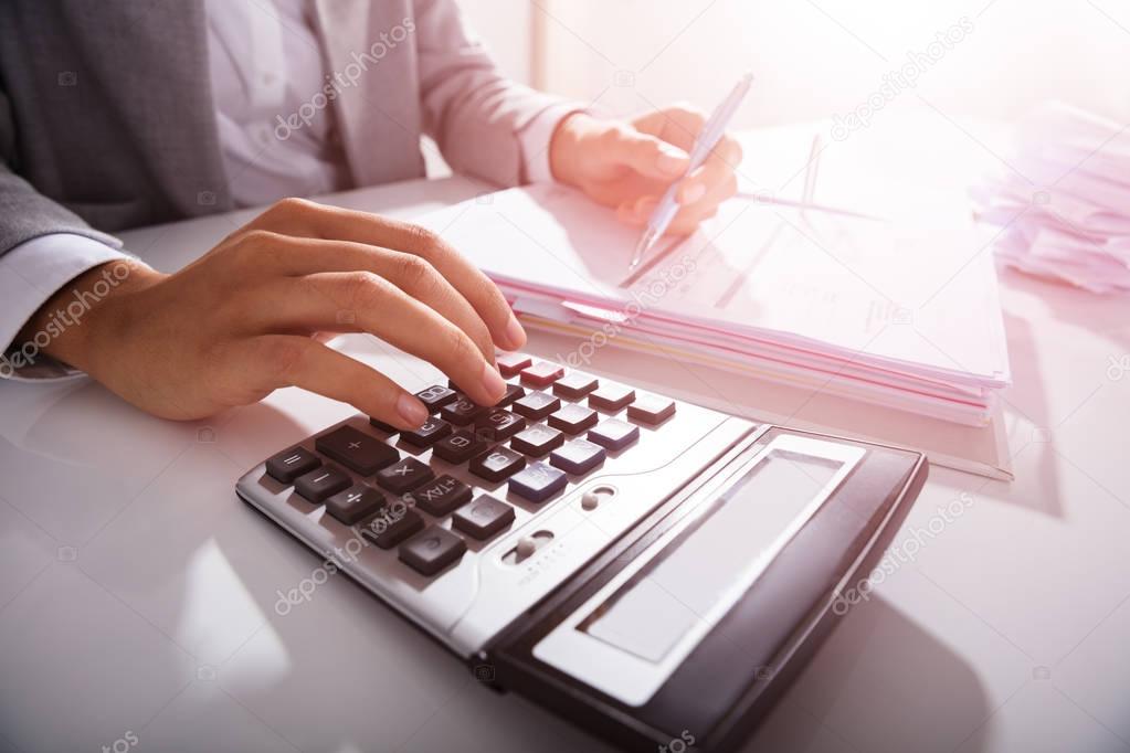 Close-up Of Businessperson Calculating Bills With Calculator In Office