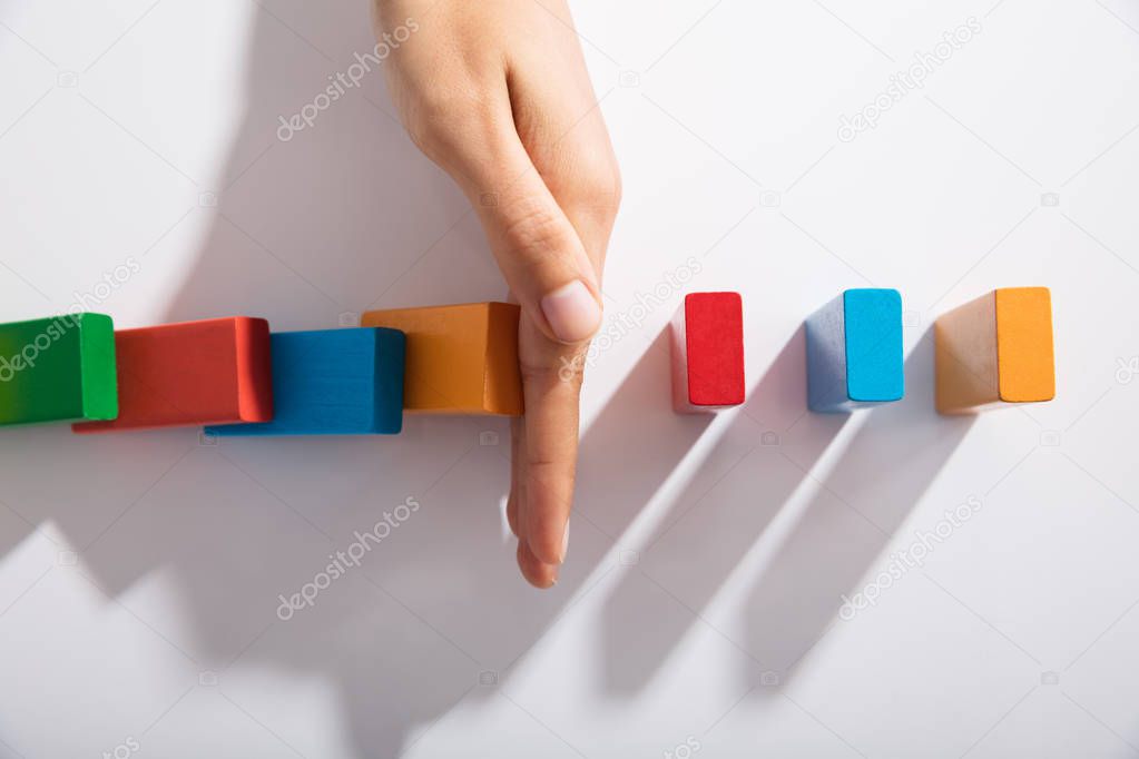 Close-up Of Businessperson Hand Stopping Colorful Blocks From Falling On Table In Office