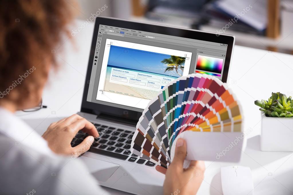 Close-up Of A Female Designer Holding Colorful Swatch Working On Laptop In Office