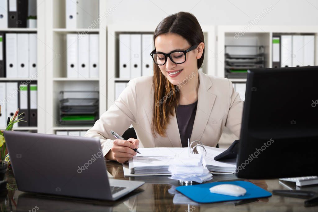 Happy Young Businesswoman Using Calculator At Workplace