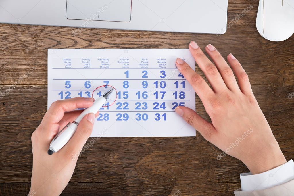 Close-up Of A Businessperson's Hand Drawing Red Circle On Calendar Date With Pen