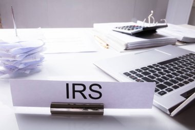 Close-up Of IRS Nameplate On Desk With Laptop And Documents clipart