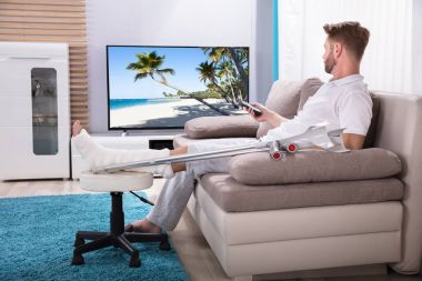 Kırık bacak evde televizyon izlerken koltukta oturan adam