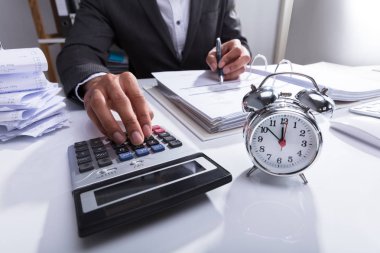 Business sperson, Masadaki Alarm Saati ile Bill 'i Hesaplamak için Hesap Makinesi Kullanıyor