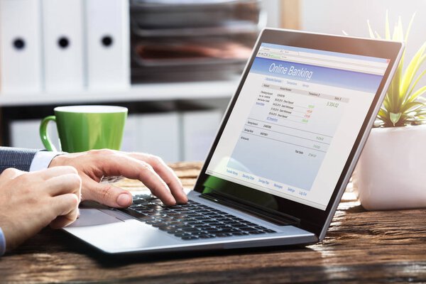 Close-up Of A Businessperson's Hand Doing Online Banking On Laptop Over Wooden Desk