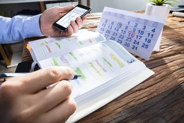 生意人的手拿着智能手机与甘特图在屏幕上 当计划日程表在日志 — 图库照片