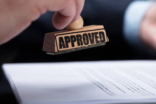 Close-up Of A Businessperson's Hand Stamping On Approved Contract Form