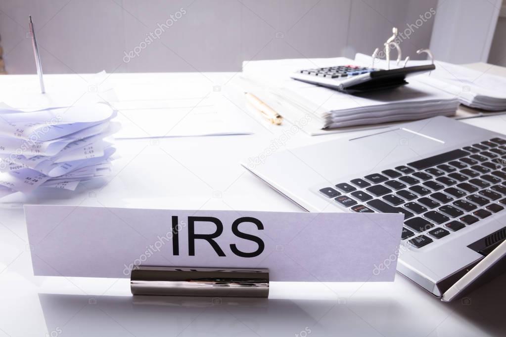 Close-up Of IRS Nameplate On Desk With Laptop And Documents