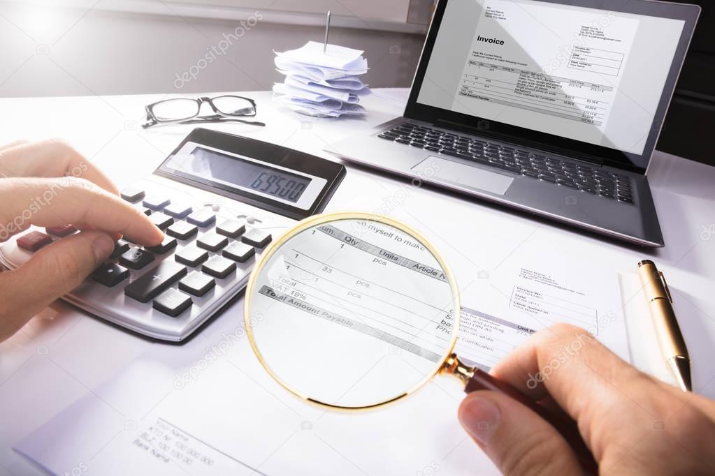 High Angle View Of A Businessperson Analyzing Bill With Magnifying Glass In Office