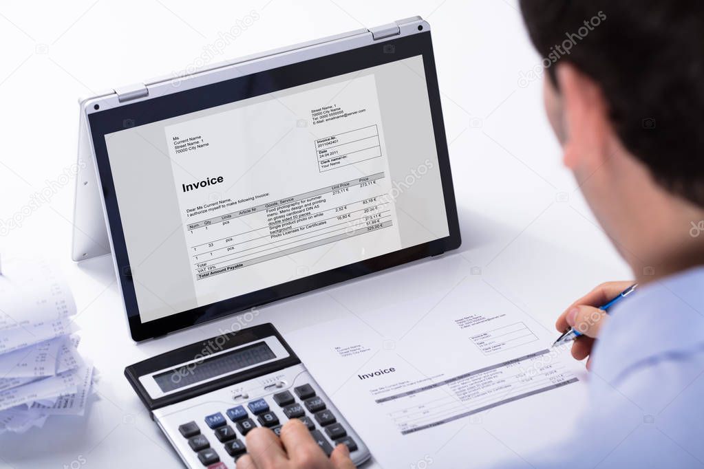 Close-up Of Businessman Calculating The Invoice Using Hybrid Laptop And Calculator At Workplace
