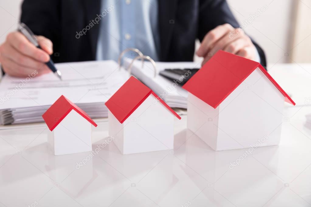 Businessperson Calculating Bill Behind Different Size Of House Model In A Row