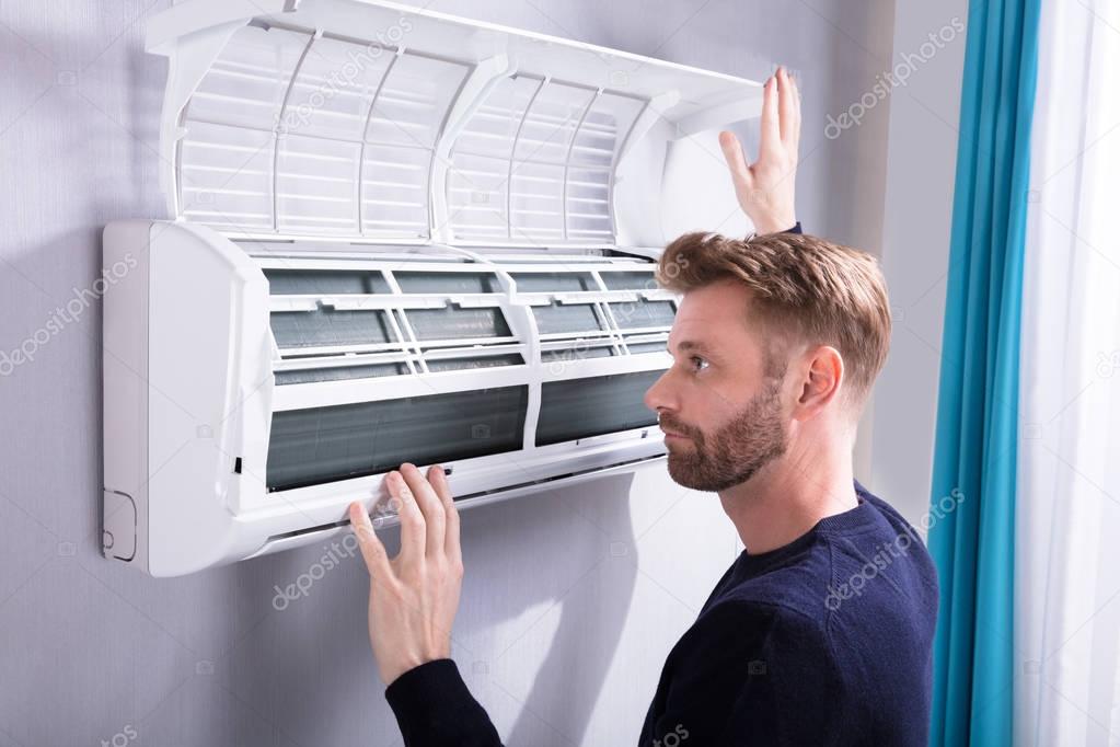 Close-up Of A Young Man Checking Air Conditioner Mounted On Wall